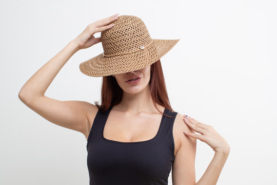 Red-haired girl in a black t-shirt and straw hat posing on a white background