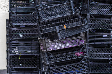 Piles of black plastic boxes for fruits and vegetables. Used boxes against the wall outdoors....