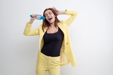 Red-haired girl in a yellow suit sings into a microphone on a white background
