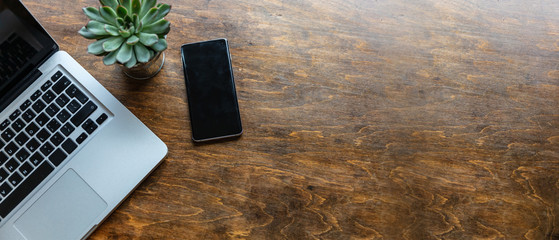 Workplace. Computer laptop and mobile phone on a wood office desk, top view