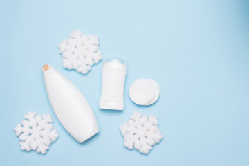 Winter body care products on blue background with snow, copyspace