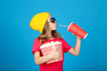 Young girl with popcorn in bucket and paper cup on blue background