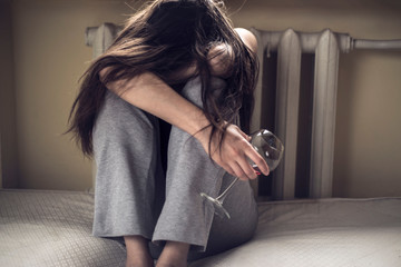 female alcoholism problem concept. A young girl sits in a dirty room, with tousled hair, and a...