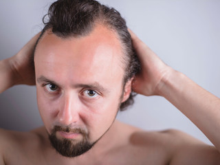 Obraz premium Portrait of a young guy with magnificent hair that falls early on his forehead. The problem of premature aging. Combing hair and indignantly looking in the mirror