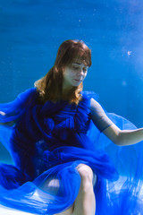 Fototapeta na wymiar Beautiful girl in a blue dress swims underwater in the pool or in the sea.