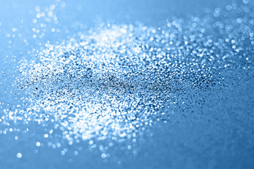 Splash of silver sparkles on classic blue background. Blurry image. Classic blue color of 2020.
