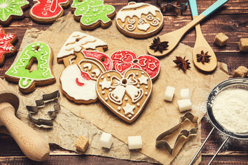 Christmas gingerbread cookies with kitchen utensils, flour and sugar cubes on brown wooden table