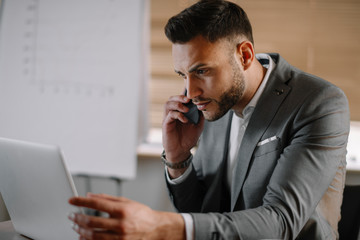 Handsome businessman in office talking on phone. Successful man in suit discussing business on phone call. 