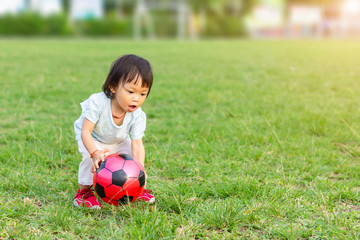 Happy Asian baby child girl playing and​ picking up a​ ball toys at the field playground. She...