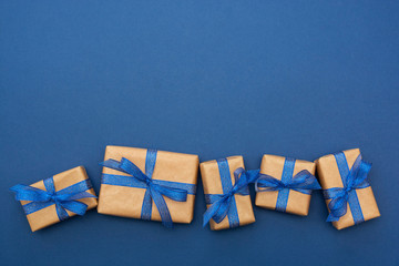 Craft paper wrapped gift boxes in a row on blue background, flat lay with copy space. Christmas abstract mock up.