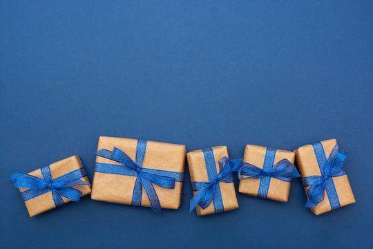 Craft paper wrapped gift boxes in a row on blue background, flat lay with copy space. Christmas abstract mock up.