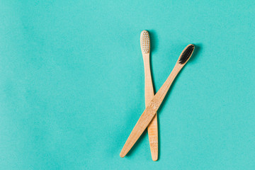Two wooden bamboo eco friendly toothbrushes on aquamarine background. Dental care and zero waste concept. Flat lay, top view, copy space.
