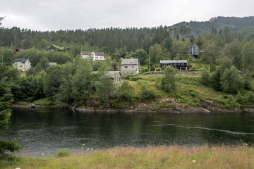 Fototapeta na wymiar spaced out houses in wood on river waters, near Evanger , Norway