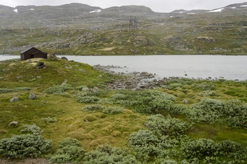 Fototapeta na wymiar isolated house on mountain lake shore under low clouds, near Finse, Norway