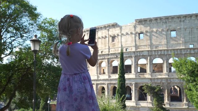 Cute Little Girl in Violet Dress Taking Photos of Coliseum or Colosseum with Smartphone in Rome. Slow Motion. Concept of Holidays, Vacations and Travel in Europe