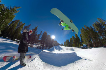 SELFIE: Woman takes a selfie while snowboarder jumps off kicker and does a trick