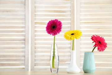 Ceramic vases with gerbera flowers on wooden background