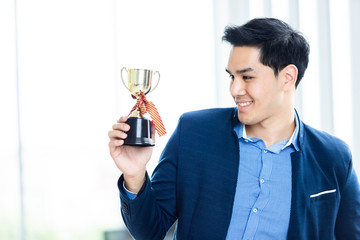 Portrait of successful feeling winner screaming handsome young asian businessman holding a champion cup at In the office room background.