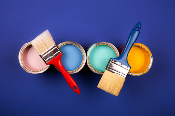 Four open cans of paint with brushes on blue background. Yellow, blue, pink, turquoise colors of paint. Top view.