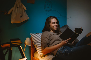 woman relaxing in her room reading book and drinking coffee or tea