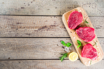 Beef meat steaks with spices, old wooden background with cutting board top view copy space