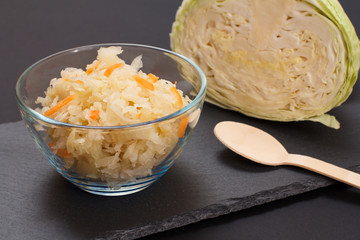 Fermented cabbage with herbs and spices in glass bowl on the black background