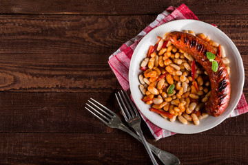 Beans with grilled sausages on wooden background