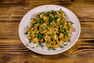 Plate with champignons stewed in sour cream on a wooden table