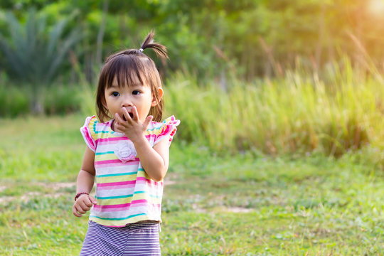 Portrait image of baby 1-2 years old. Asian child girl put her hands and in her mouth and biting her fingers at the playground. Personal hygiene and kid healthy concept.