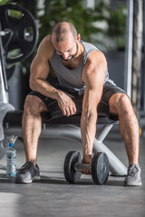 Fototapeta na wymiar Muscular man practicing with dumbbells in fitness gym