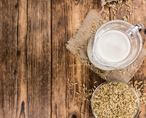 Old wooden table with fresh Oat Milk (close-up shot; selective focus)