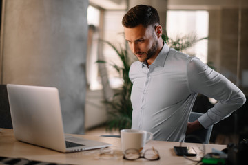 Obraz premium Portrait of handsome businessman in office. Tired businessman working on laptop in office .