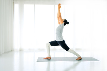 Side view portrait of beautiful young woman doing yoga or pilates exercise. Standing in Warrior one pose, Virabhadrasana, working out,In the white room indoor full length