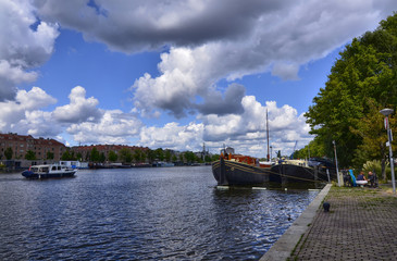 Fototapeta na wymiar Amsterdam, Holland, August 2019. View of the Amstel River, outskirts of the city. A large moored boat is used as a houseboat. Sunny day with blue sky and white clouds.