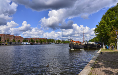 Fototapeta na wymiar Amsterdam, Holland, August 2019. View of the Amstel River, outskirts of the city. A large moored boat is used as a houseboat. Sunny day with blue sky and white clouds.