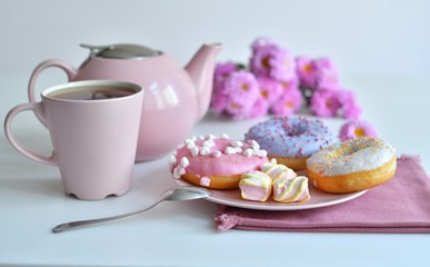 pink teapot, cup of tea and colorful delicious doughnuts