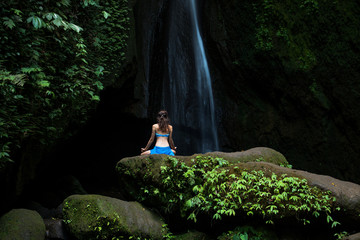 Young woman sitting on the rock, practicing yoga near waterfall. Hands in gyan mudra. Leke Leke...