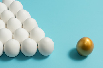 Concept of individuality, exclusivity, better choice. One golden egg among white eggs on blue background.