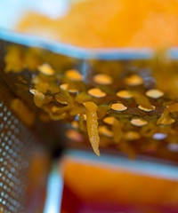 A woman's hand holds a piece of fresh pumpkin and rubs it on a metal kitchen grater.
