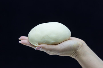 Baker's hands round dough on a black background.