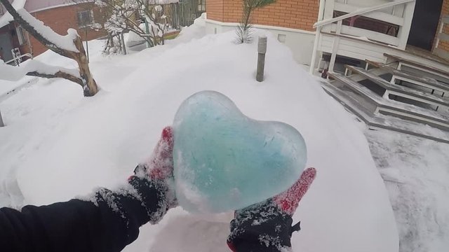 A man takes out a blue icy heart from a snowdrift. It clears the ice of snow. First-person view.