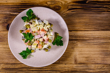 Ceramic plate with russian traditional new year salad olivier on a wooden table. Top view