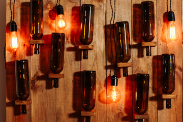 wine bottles hanging on a wooden wall with old edison lamps