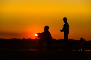Naklejka na ściany i meble Child silhouette playing fun with many friends and playing against the sunset.