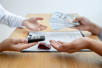 Car rental and Insurance concept, Young salesman receiving money and giving car's key to customer after sign agreement contract with approved good deal for rent or purchase