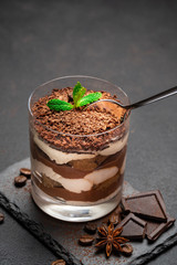 Classic tiramisu dessert in a glass cup and pieces of chocolate on stone cutting board on darl concrete background