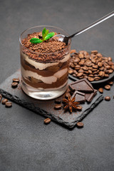 Classic tiramisu dessert in a glass cup and pieces of chocolate on stone cutting board on darl concrete background