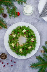 Olivier salad Christmas wreath with vegetables, meat (sausage), eggs and mayonnaise on a plate on a gray background.  Traditional festive Russian and Ukrainian salad for Christmas and New Year.