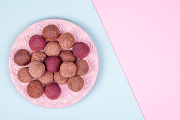 Obraz na płótnie Canvas Homemade Raw Vegan Cacao Energy Balls on Vintage Plate on Trend Blue and Pink Paper Background. Healthy Chocolate Snacks from Nuts and Dates. Concept of Natural Vegetarian Handmade Dessert