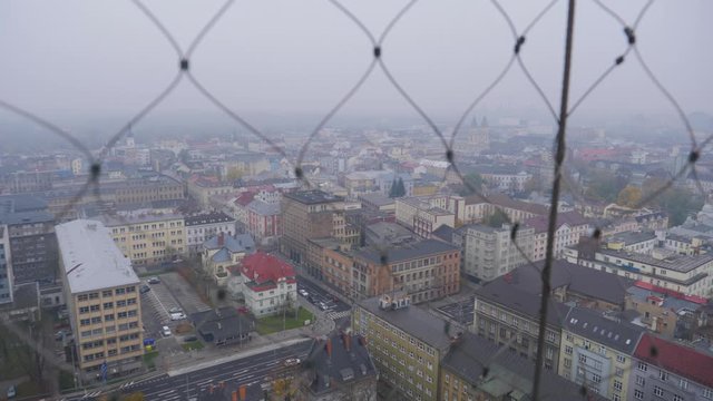 Pan looking out at the city of Ostrava on a cloudy day through a wire fence from the top of the New Town Hall 